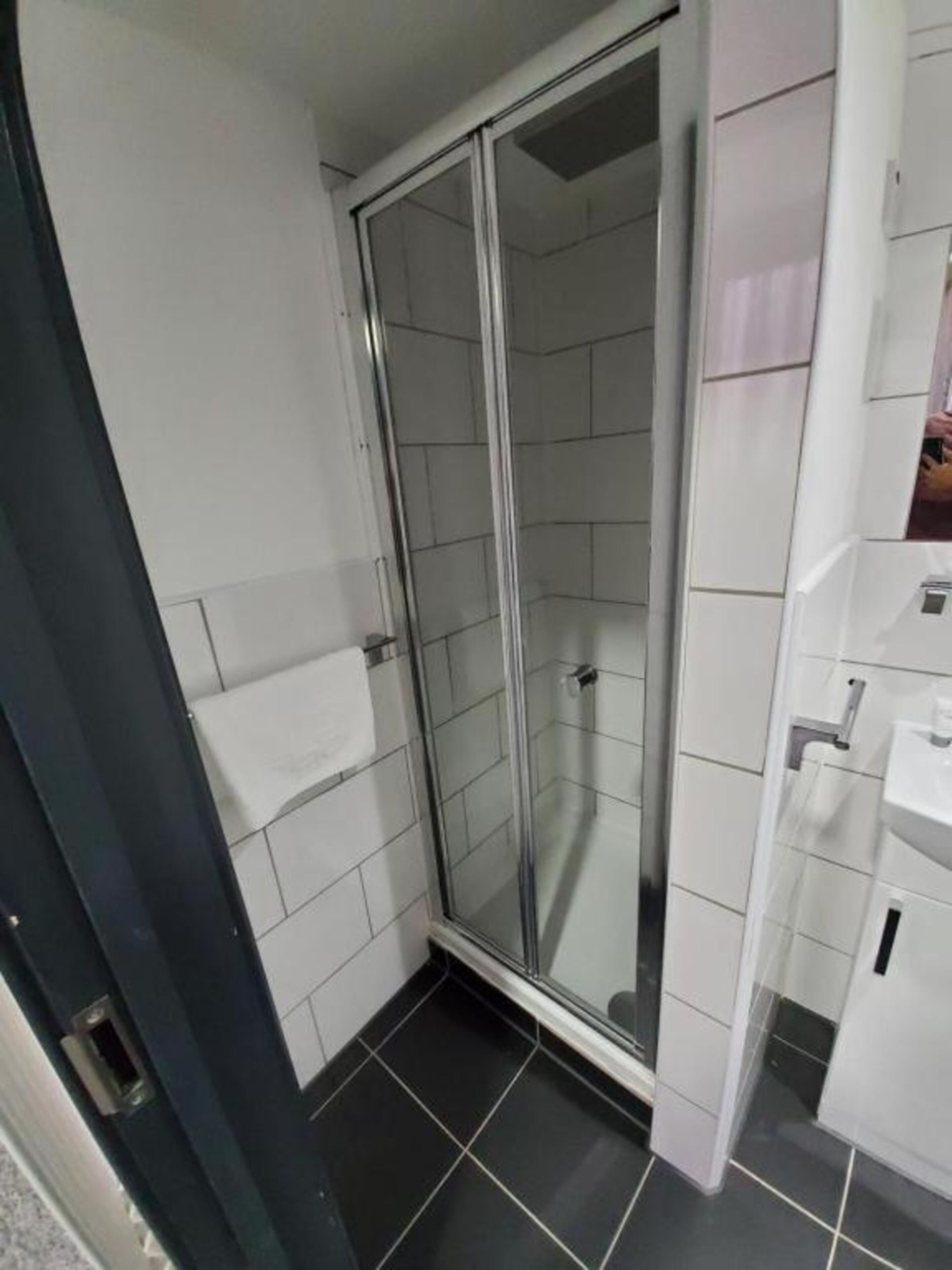 Ein Badezimmer mit Duschkabine aus Glas, weißen Fliesenwänden und einem schwarzen Fliesenboden.