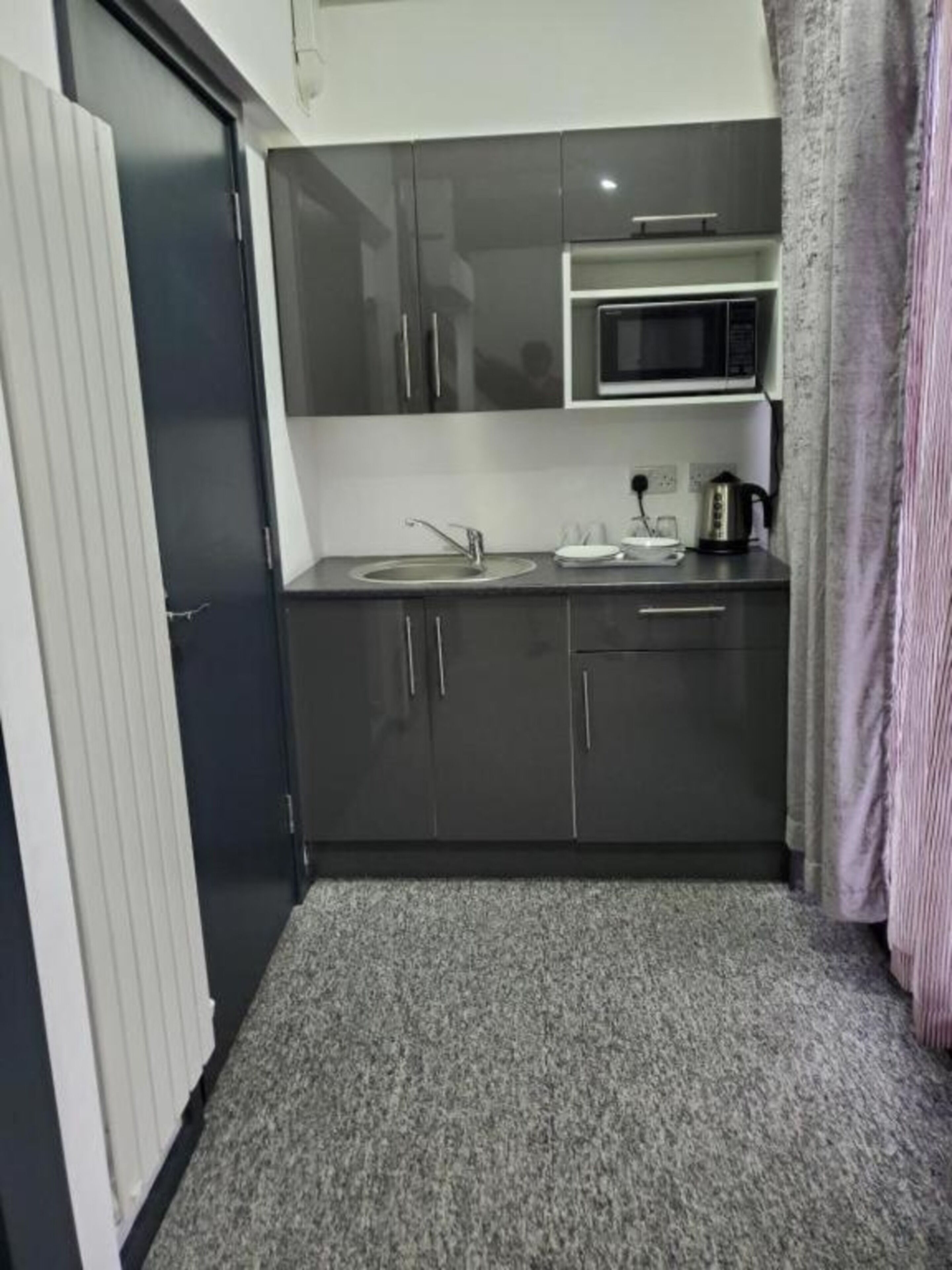 A compact kitchen with dark cabinets, a microwave, a sink, and a kettle.