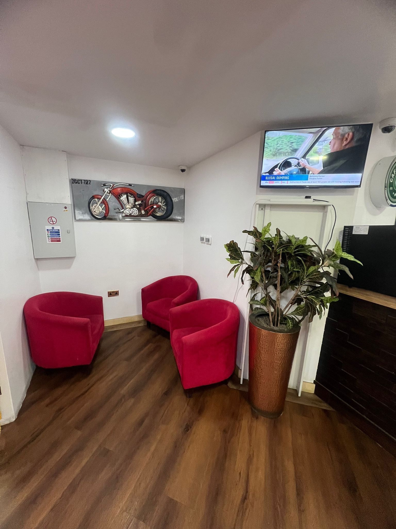 Ein Empfangsbereich mit montiertem Fernseher, einem Motorrad-Kunstwerk und drei roten Stühlen.