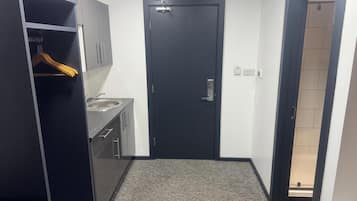 A compact room with a dark door, a small sink, and a wardrobe with a hanging rack.