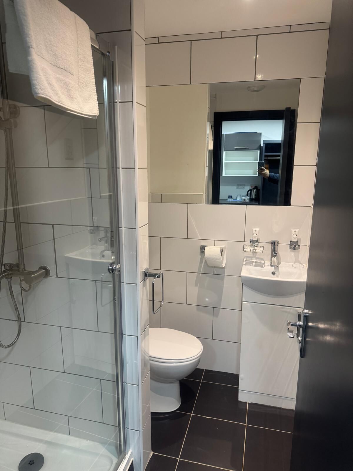 Un baño moderno con ducha de vidrio, inodoro blanco, lavamanos con espejo y una toalla colgada en la pared.