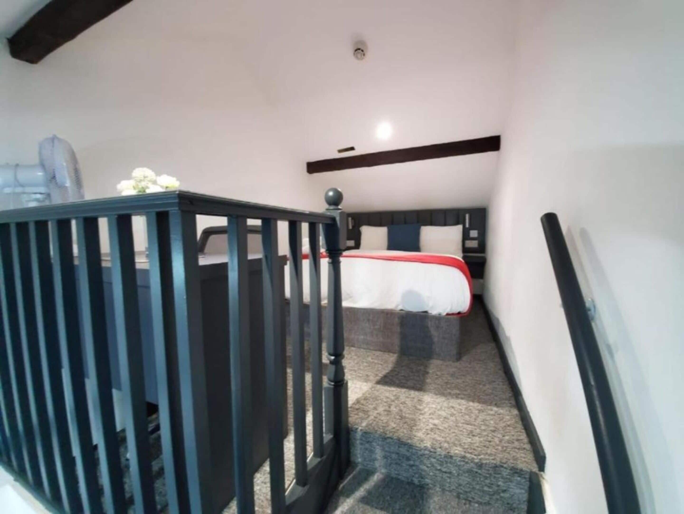 A bedroom with a bed, a nightstand, a dresser, and a staircase with a railing.
