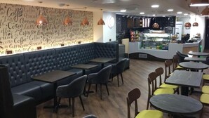 Una cafeteria amb zona de seients que inclou un banc amb coixins blaus i taules, una paret amb paraules relacionades amb el cafè, i un mostrador amb vitrina expositora.