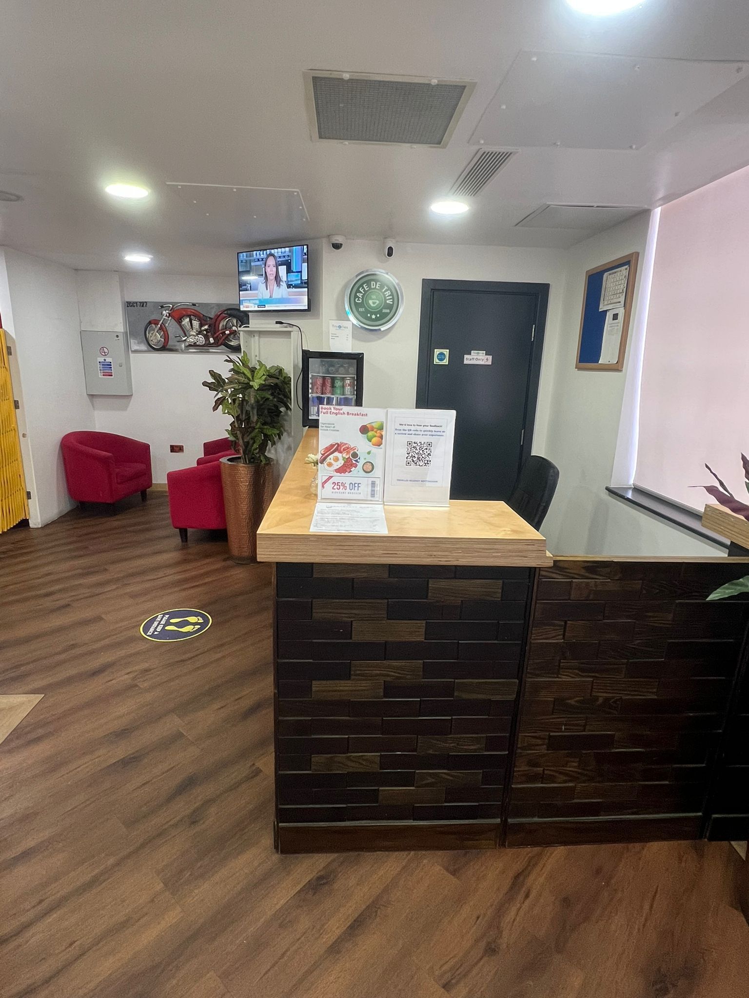 A reception area with a wooden reception desk, red chairs, a potted plant, a mounted television, and a wall clock.