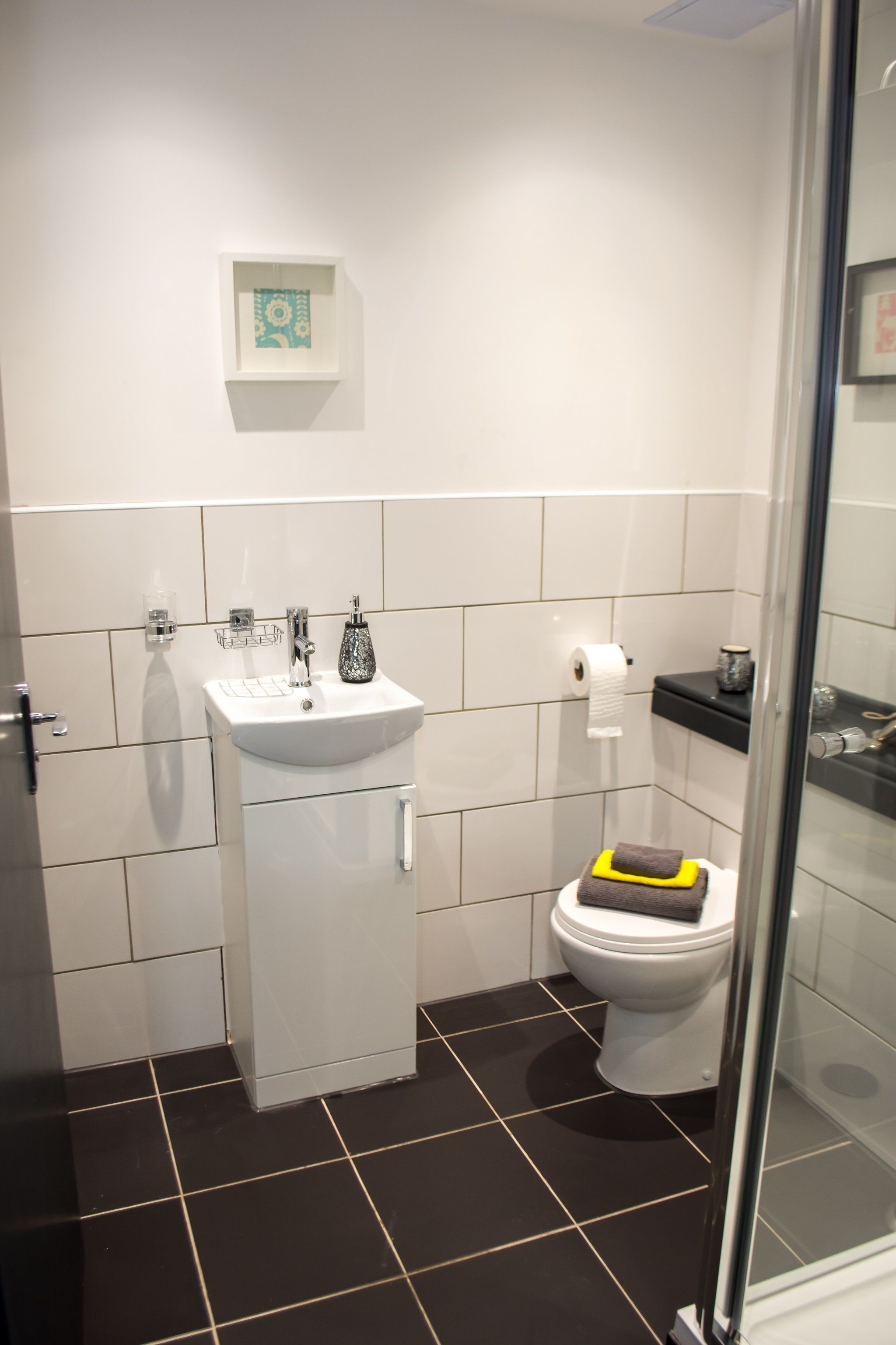 Un baño moderno con lavabo blanco, inodoro y cabina de ducha con mampara de vidrio.