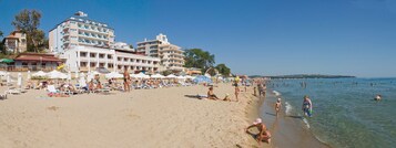Una playa con varios edificios de hotel, tumbonas, sombrillas y gente disfrutando del agua.