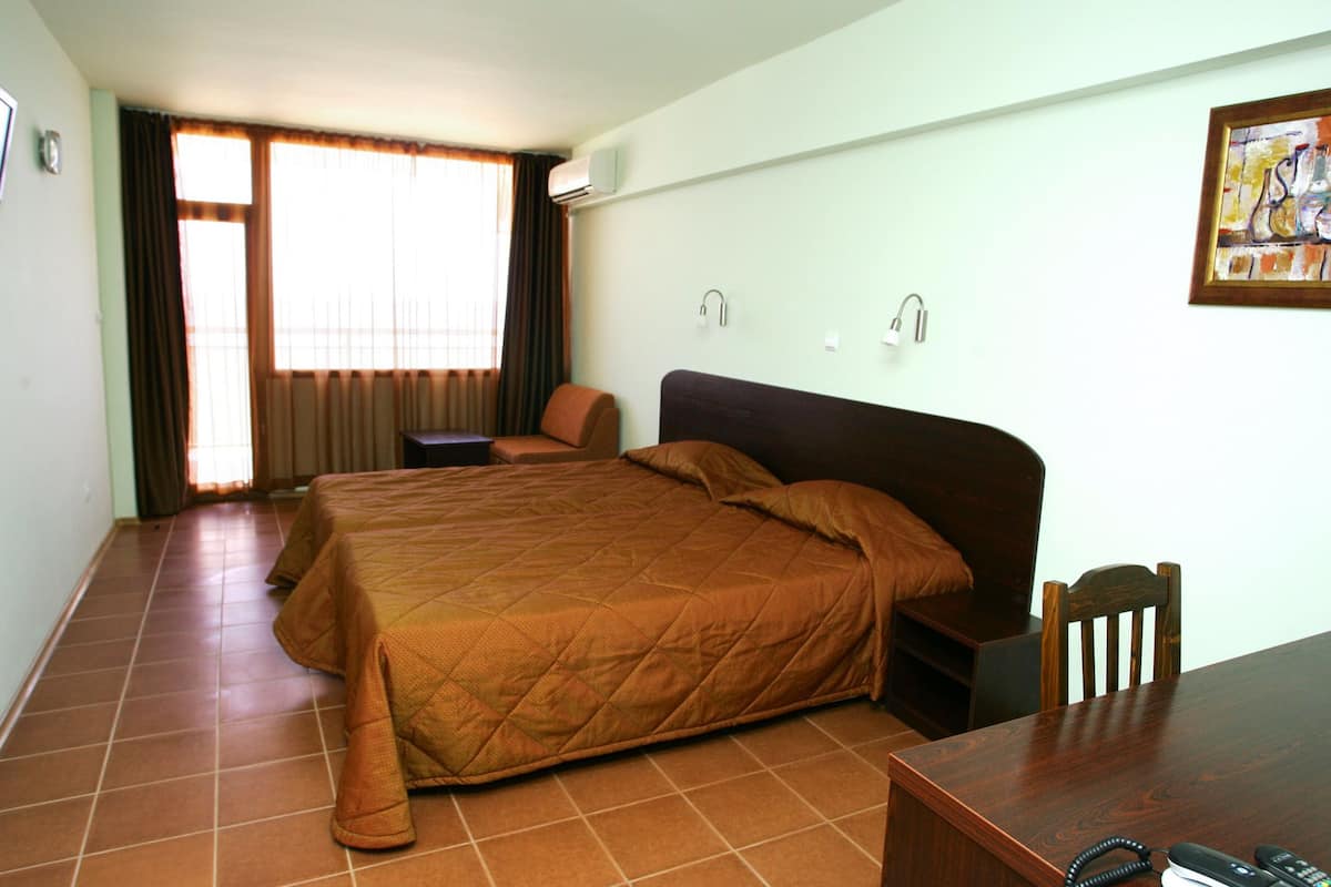 A hotel room with a large bed, a wooden desk, a chair, and a window with curtains.