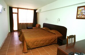 Una habitación de hotel con una cama grande, un escritorio de madera, una silla y un ventanal con cortinas.