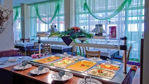 A buffet setup with multiple food stations, tables, chairs, and a large window with green drapes. - Paraizo Beach - All Inclusive (Obzor)