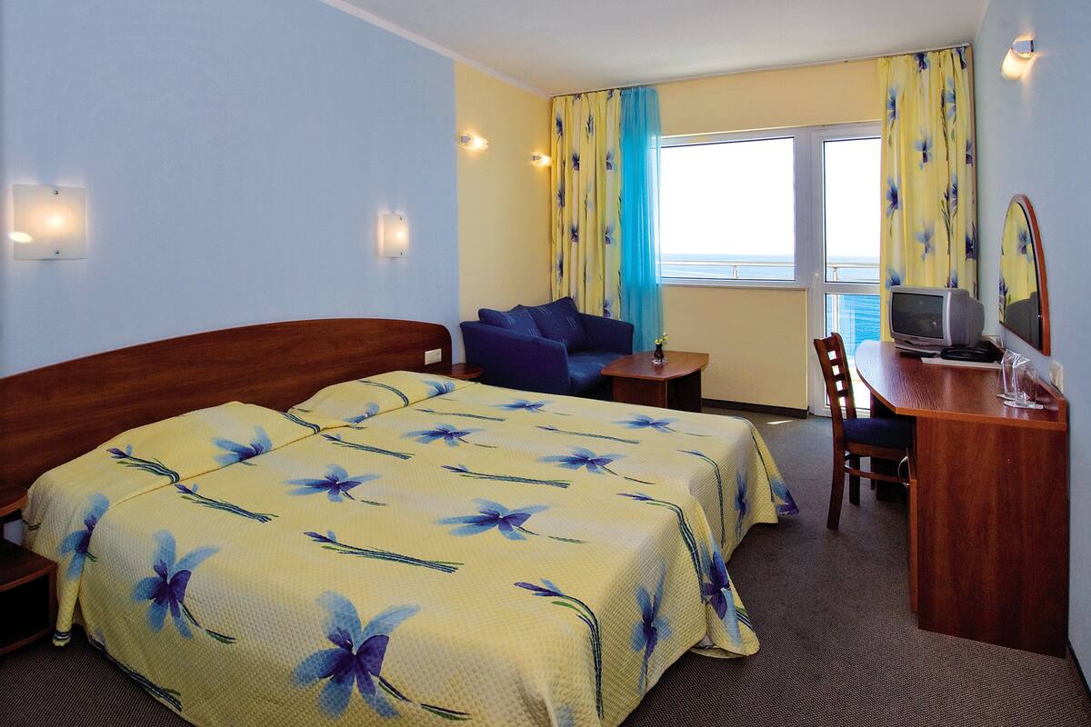 A hotel room with two beds, a desk with a television, and a window with curtains.
