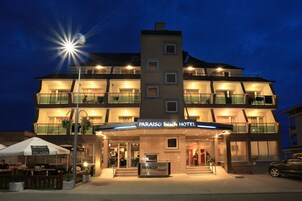 Un hotel de varios pisos con una entrada destacada, zona de estar al aire libre y un letrero que indica que es el Paraiso Beach Hotel.