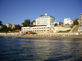 Un hotel de varios pisos con balcones, cerca de una playa con sombrillas y gente.