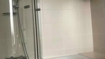 A modern bathroom with a glass-enclosed shower, a white bathtub, and a towel rack with folded towels.