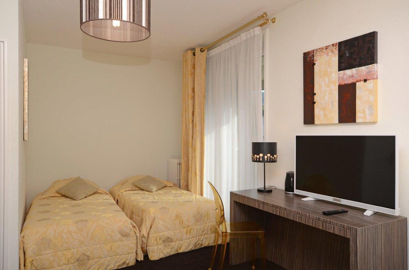 A hotel room with two beds, a desk with a TV, a lamp, and a painting on the wall.