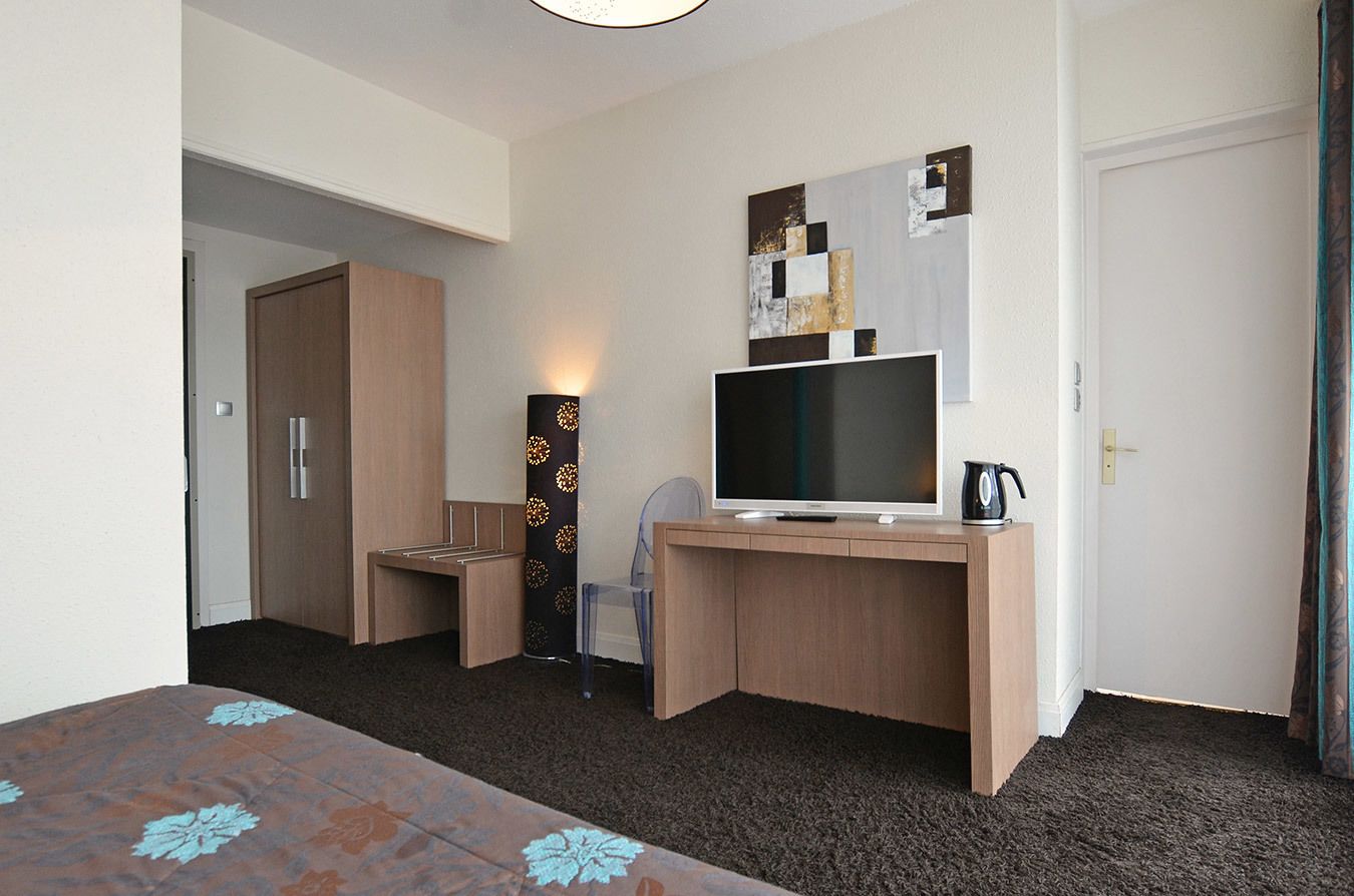 Habitación de hotel con escritorio de madera, televisor de pantalla plana, cafetera y una obra de arte colgada en la pared.
