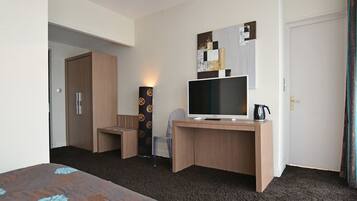 Habitación de hotel con escritorio de madera, televisor de pantalla plana, cafetera y una obra de arte colgada en la pared.