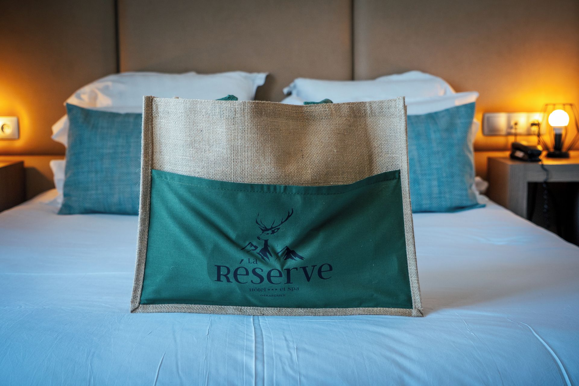 A bed with a green pillow featuring a deer logo and the word 'Reserve' on a hotel bed.