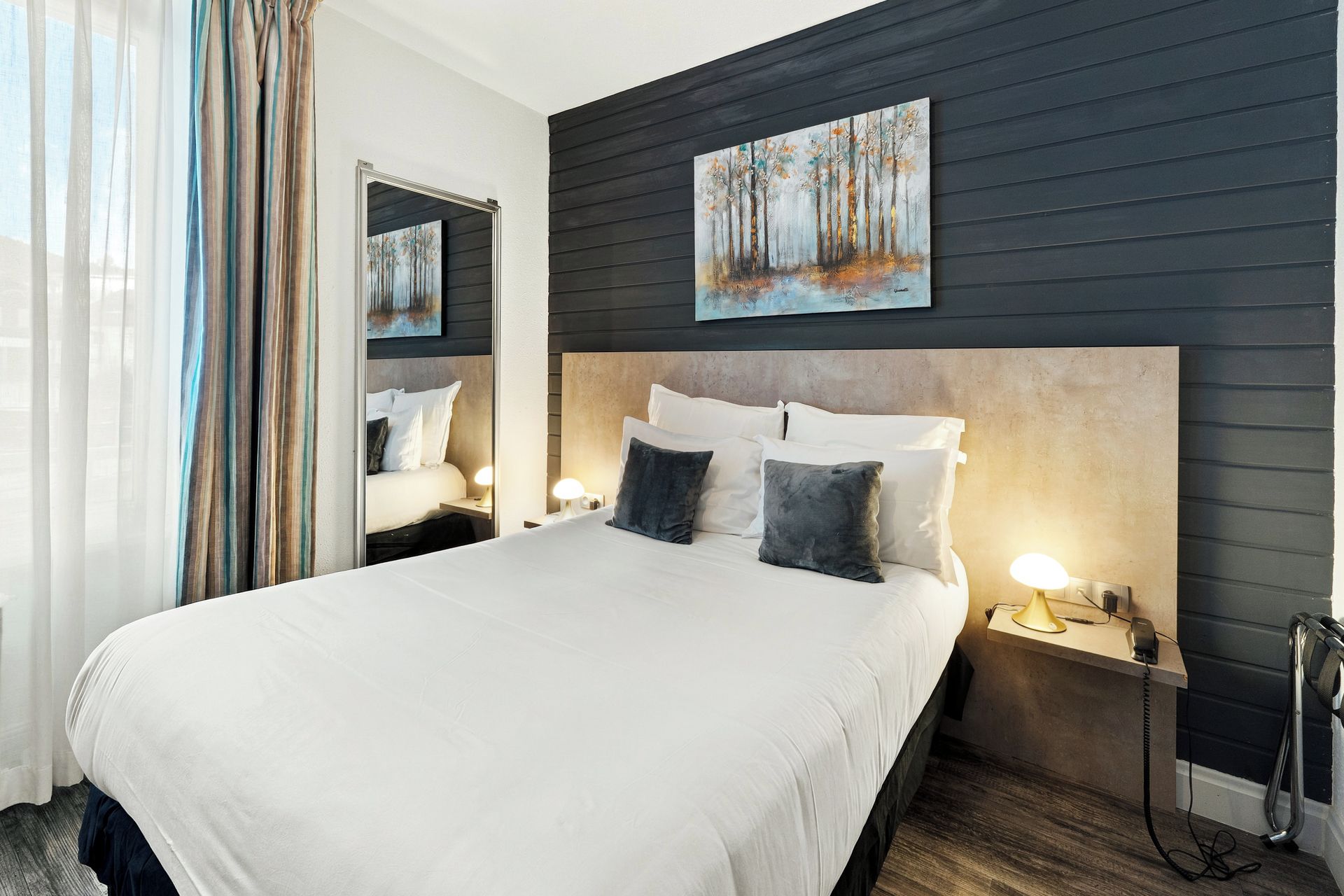 Habitación de hotel con una cama grande, cabecera, mesitas de noche con lámparas, un espejo y un cuadro en la pared.