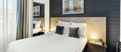 A hotel room with a large bed, a headboard, bedside tables with lamps, a mirror, and a painting on the wall.