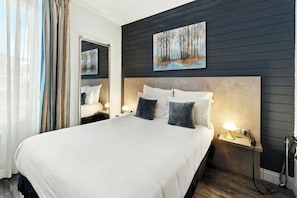Habitación de hotel con una cama grande, cabecera, mesitas de noche con lámparas, un espejo y un cuadro en la pared.
