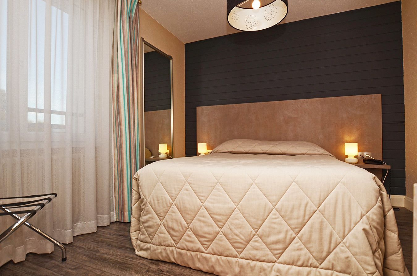 Une chambre d’hôtel avec un grand lit, une table de chevet avec une lampe et un miroir au mur.