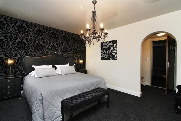 Une chambre à coucher avec un grand lit, un lustre, un banc et une porte donnant sur une autre pièce.
