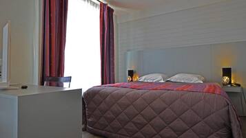 A bedroom with a large bed, a bedside table, a nightstand, and a desk.