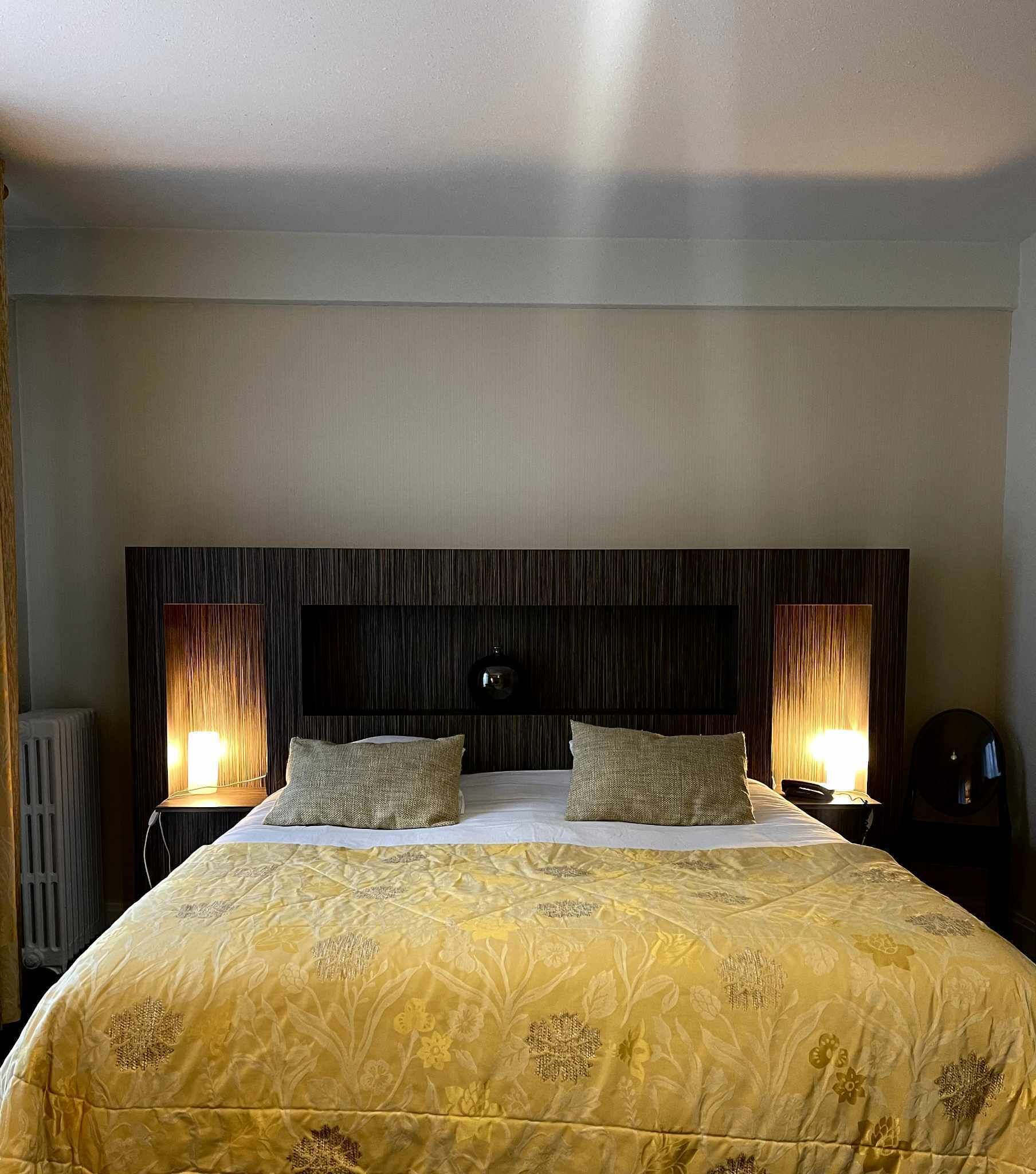 Une chambre d’hôtel avec un grand lit, deux lampes de chevet et une tête de lit en bois foncé.
