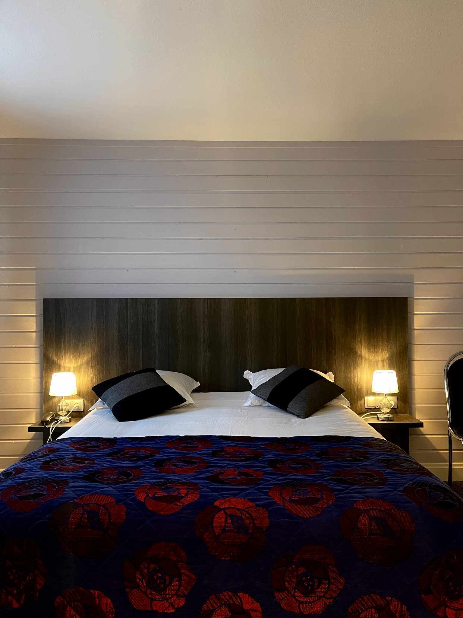 A hotel room with a large bed, two bedside lamps, and a dark wood headboard.