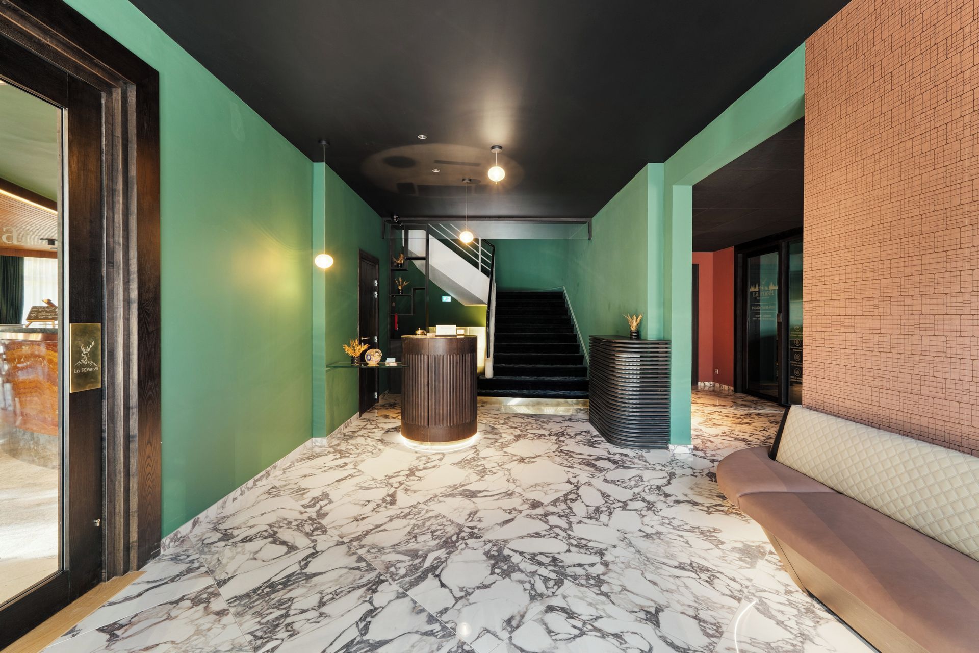 A hotel lobby with a marble floor, a staircase, and a seating area.