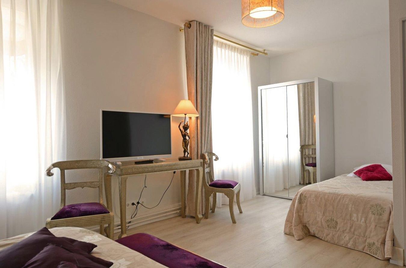 A hotel room with a bed, a desk with a television, a chair, and a lamp.