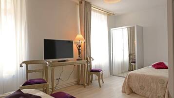 A hotel room with a bed, a desk with a television, a chair, and a lamp.