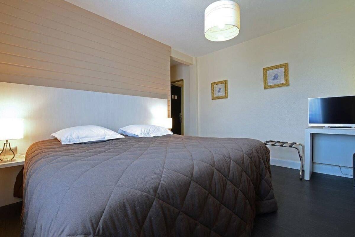 Habitación de hotel con cama, mesita de noche, lámpara, televisión y cuadros en la pared.