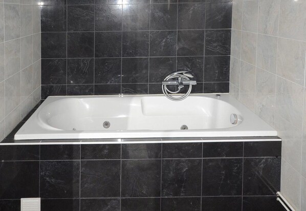 A modern bathroom with a rectangular bathtub, black marble tiles, and a chrome faucet. - Hotel la Réserve (Gerardmer)