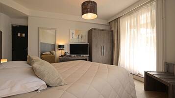 Habitación de hotel con una cama grande, un escritorio con televisor de pantalla plana, un armario y un ventanal con cortinas de gasa.