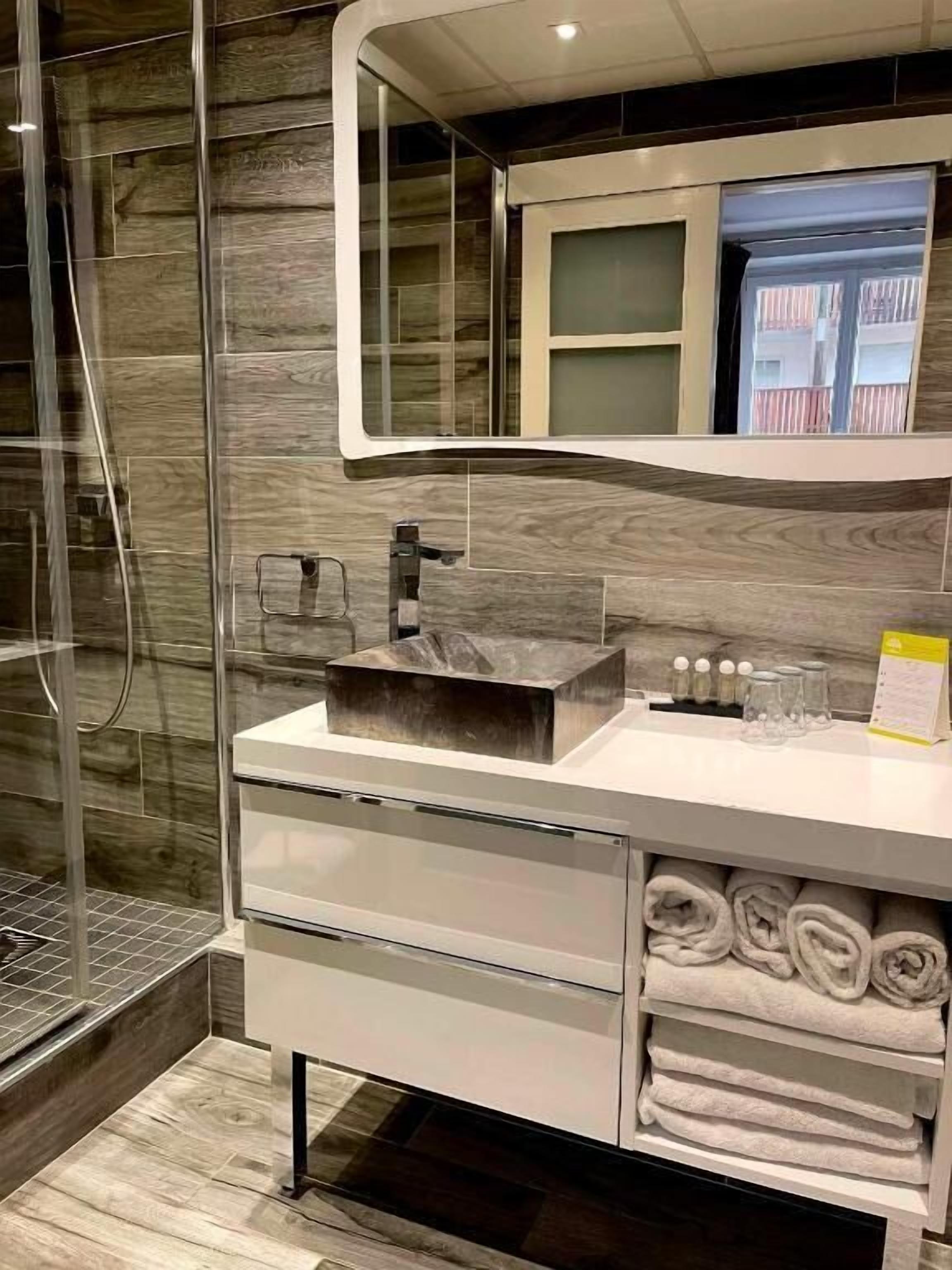 Une salle de bain moderne avec une douche à l’italienne en verre, un lavabo en marbre et des serviettes soigneusement pliées.