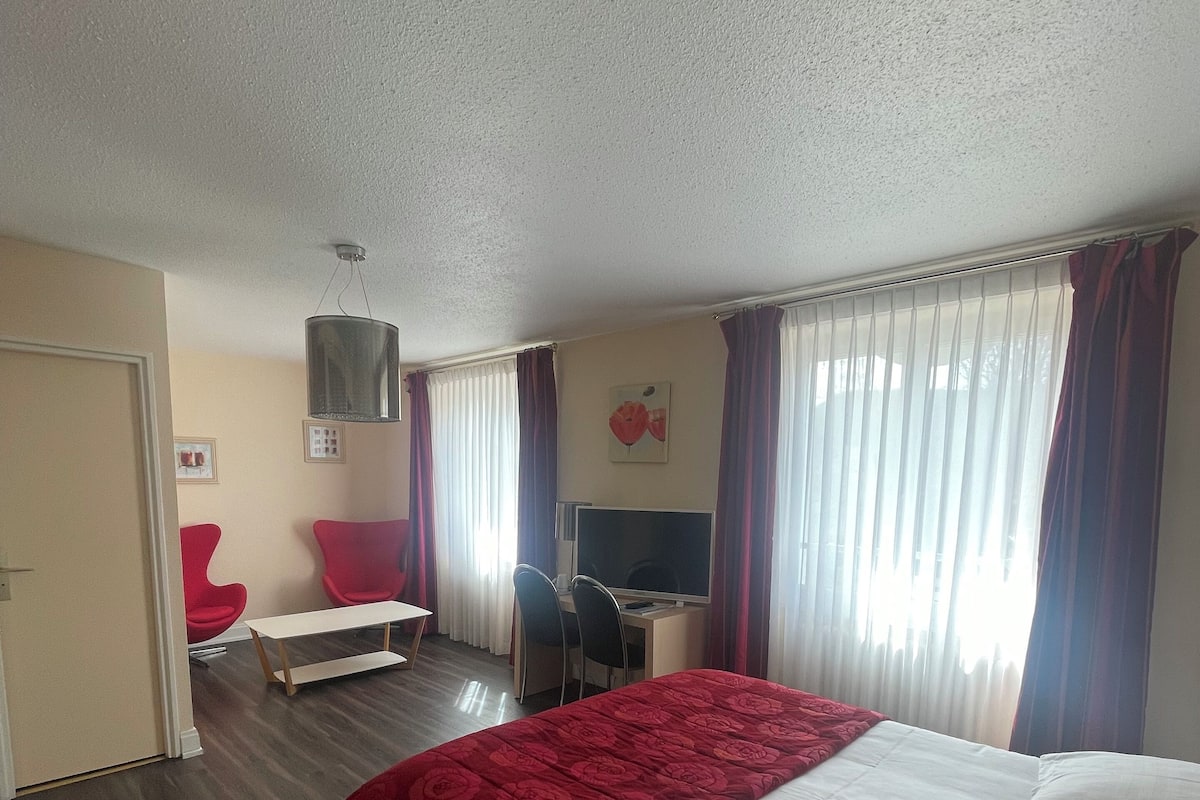 Habitación de hotel con una cama grande, un escritorio con silla, televisión y ventana con cortinas.