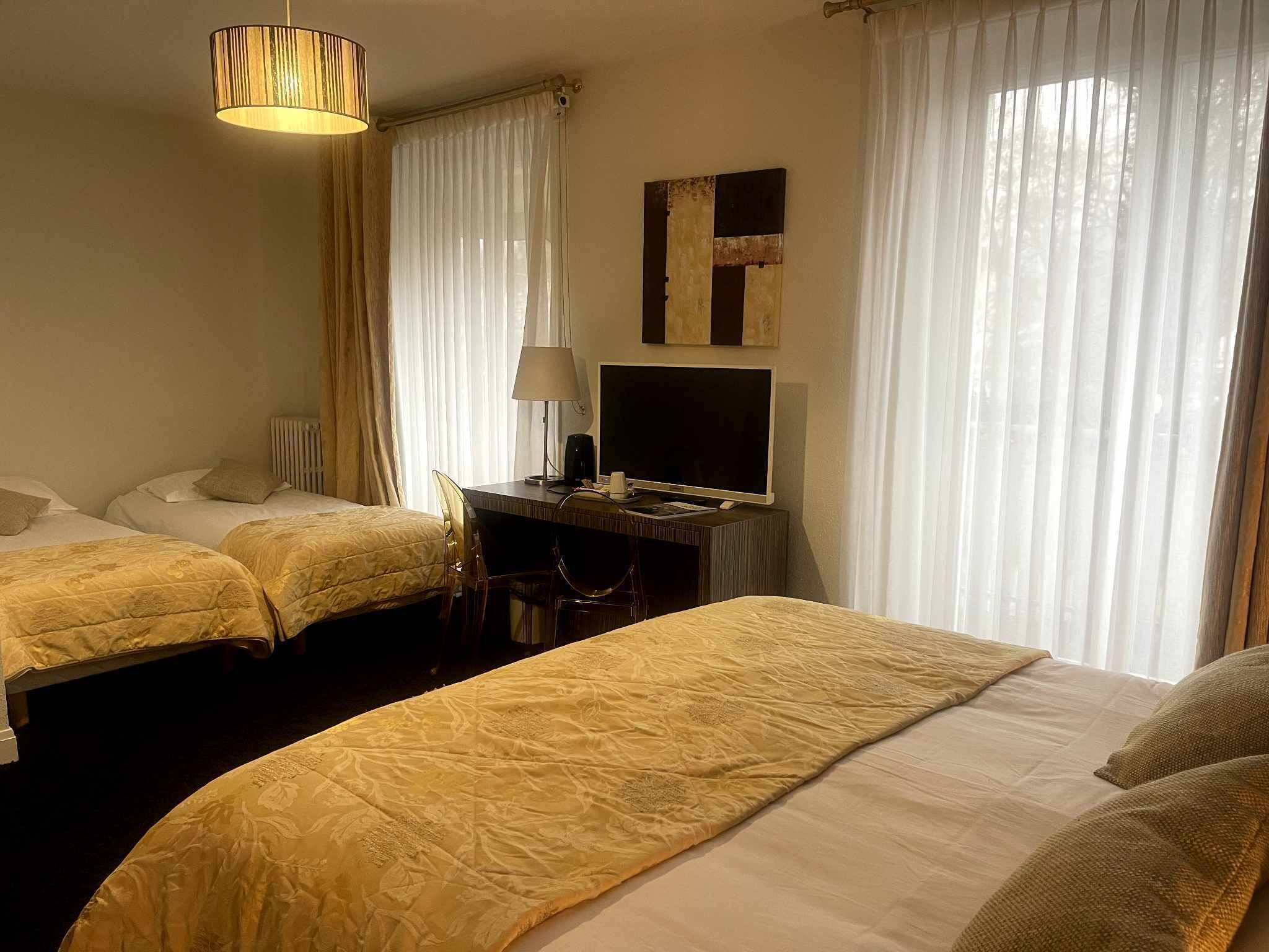 Habitación de hotel con dos camas, un escritorio con televisor y una lámpara.