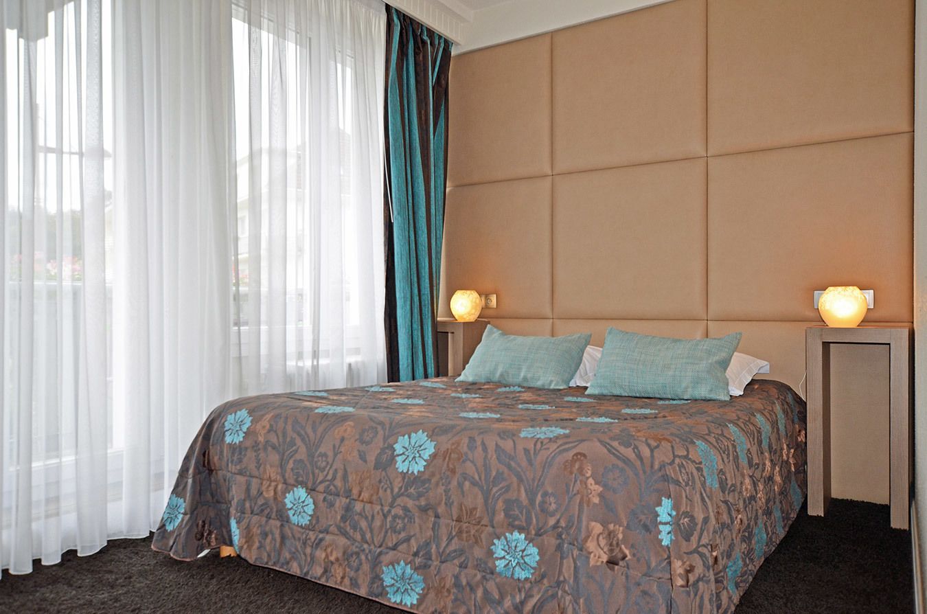 Habitación de hotel con una cama grande, dos lámparas de noche, un cabecero y cortinas translúcidas.