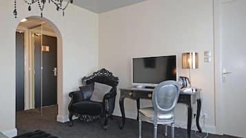 Una habitación con un sillón de cuero negro, una silla plateada, un escritorio con televisor de pantalla plana y una lámpara.