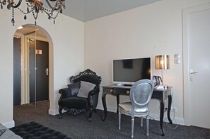 A room with a black leather armchair, a silver chair, a desk with a flat-screen TV, and a lamp. - Hotel & SPA La Réserve (Gerardmer)