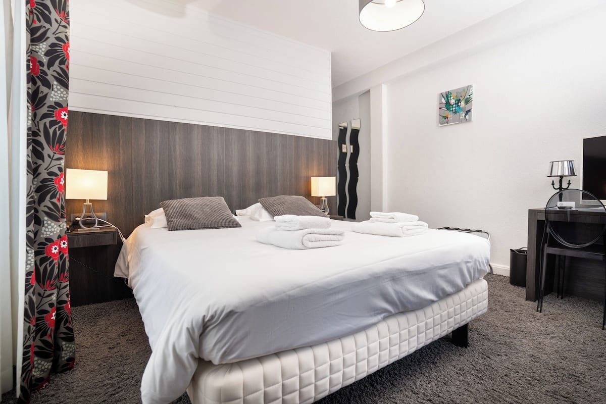 Una habitación de hotel con una cama grande, dos mesitas de noche con lámparas, un escritorio con silla y una pequeña obra de arte en la pared.