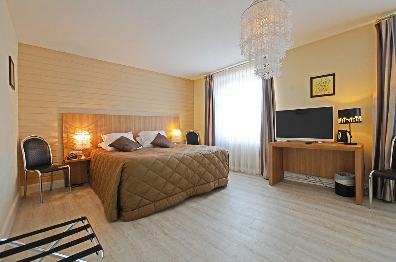 Ein Hotelzimmer mit Bett, Nachttischlampen, Fernseher, Schreibtisch und Sessel.