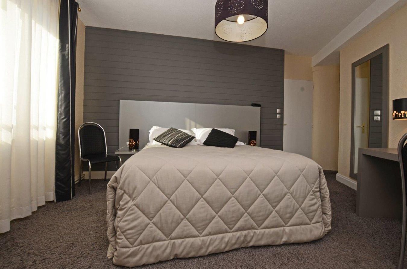 Ein Hotelzimmer mit einem großen Bett, einer Kopfteil, einem Schreibtisch mit Stuhl, einem Spiegel und einer Pendelleuchte.