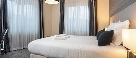 Une chambre d’hôtel avec un grand lit, une table de chevet avec une lampe et une fenêtre avec des rideaux.
