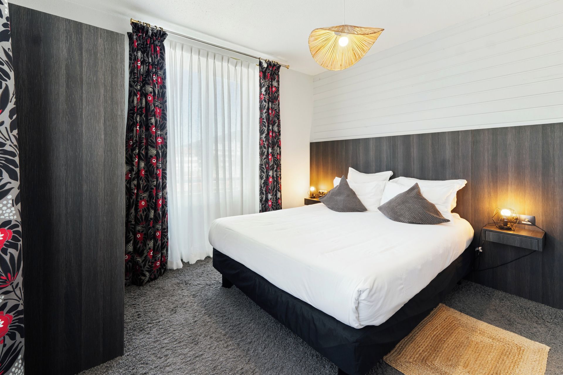 A hotel room with a large bed, dark wood headboard, white bedding, and a woven light fixture.