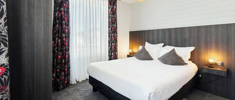 A hotel room with a large bed, dark wood headboard, white bedding, and a woven light fixture.
