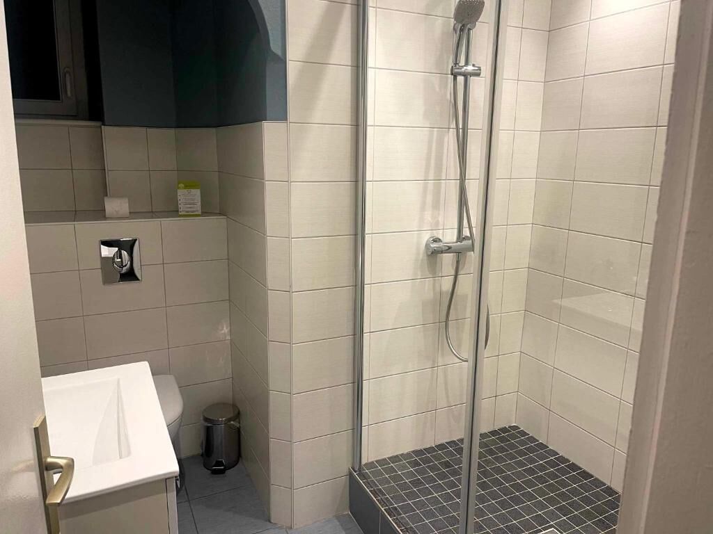 Une petite salle de bain carrelée, équipée d’une douche, de toilettes et d’un lavabo.