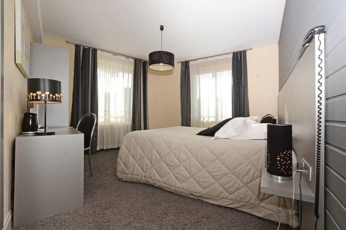 Habitación de hotel con cama, escritorio, lámpara, teléfono y cortina.