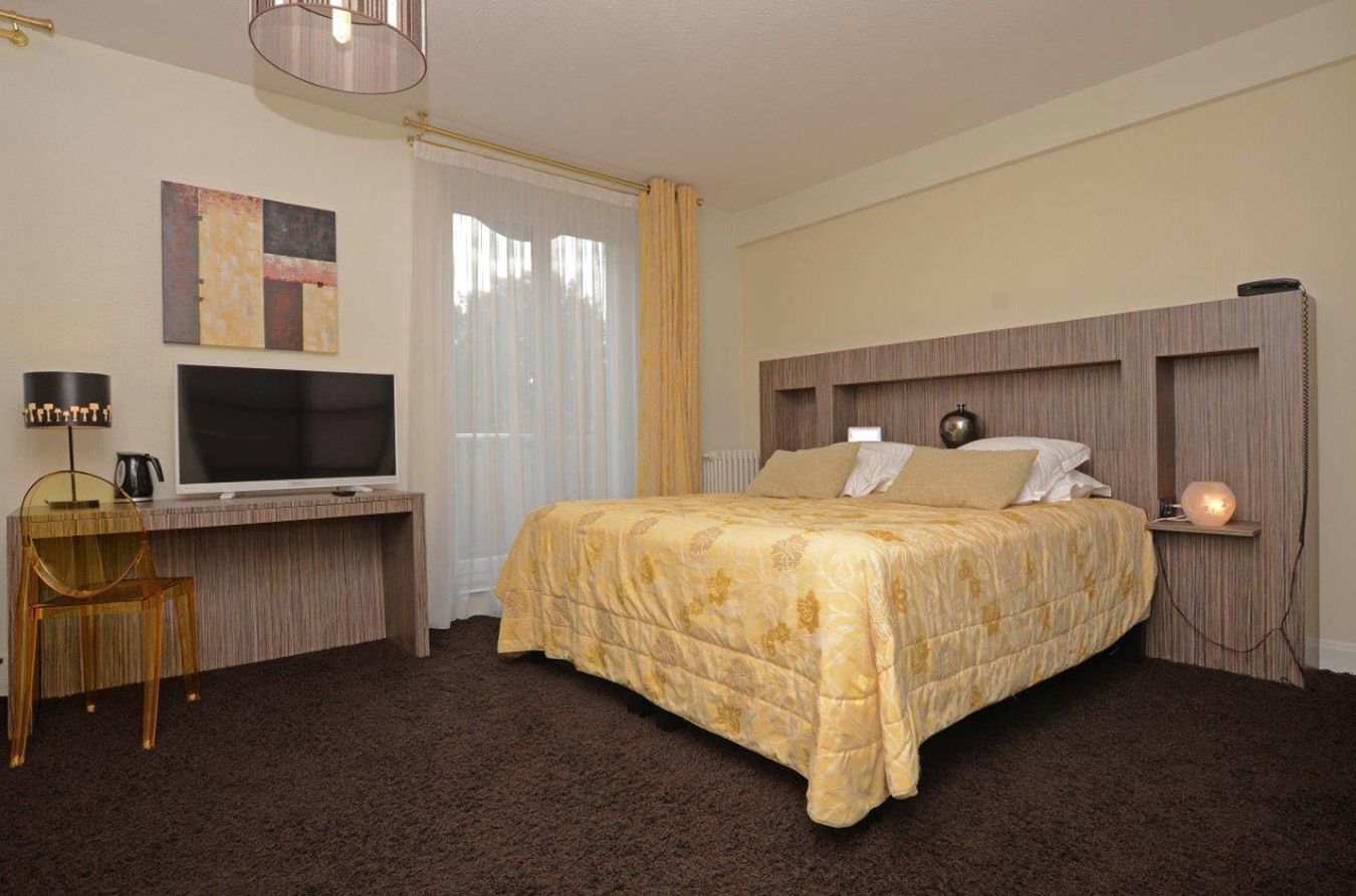 Ein Hotelzimmer mit einem Bett, einem Schreibtisch mit Fernseher, einem Sessel und einer Lampe.